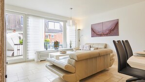 Ein modernes Wohnzimmer mit einem beigen Sofa, einem Esstisch mit Stühlen und einem großen Fenster mit Blick nach draußen.