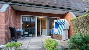 A patio with a table and chairs, a blue-striped chair, and a brick wall. - Sylter Rose - Modern 1-room apartment with terrace, parking space, WLAN. (Sylt)
