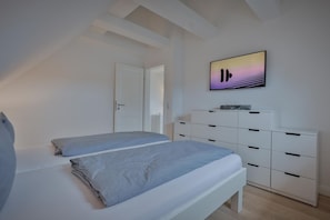 A bedroom with two beds, a white dresser, and a painting on the wall. - Sylt Seascape I - Central luxury bungalow for 4 people with sauna, garden, car (Sylt)