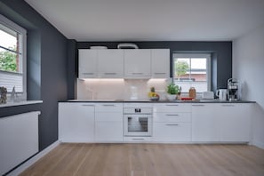 A modern kitchen with white cabinets, a built-in oven, and a window providing natural light. - Sylt Seascape I - Central luxury bungalow for 4 people with sauna, garden, car (Sylt)