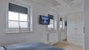 Ein Schlafzimmer mit Bett, Fernseher, Kleiderschrank und einem Fenster mit Jalousien.