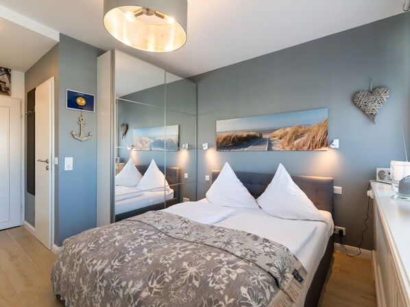 A modern bedroom with a large bed, a mirror, a painting, and a wall-mounted heart decoration.