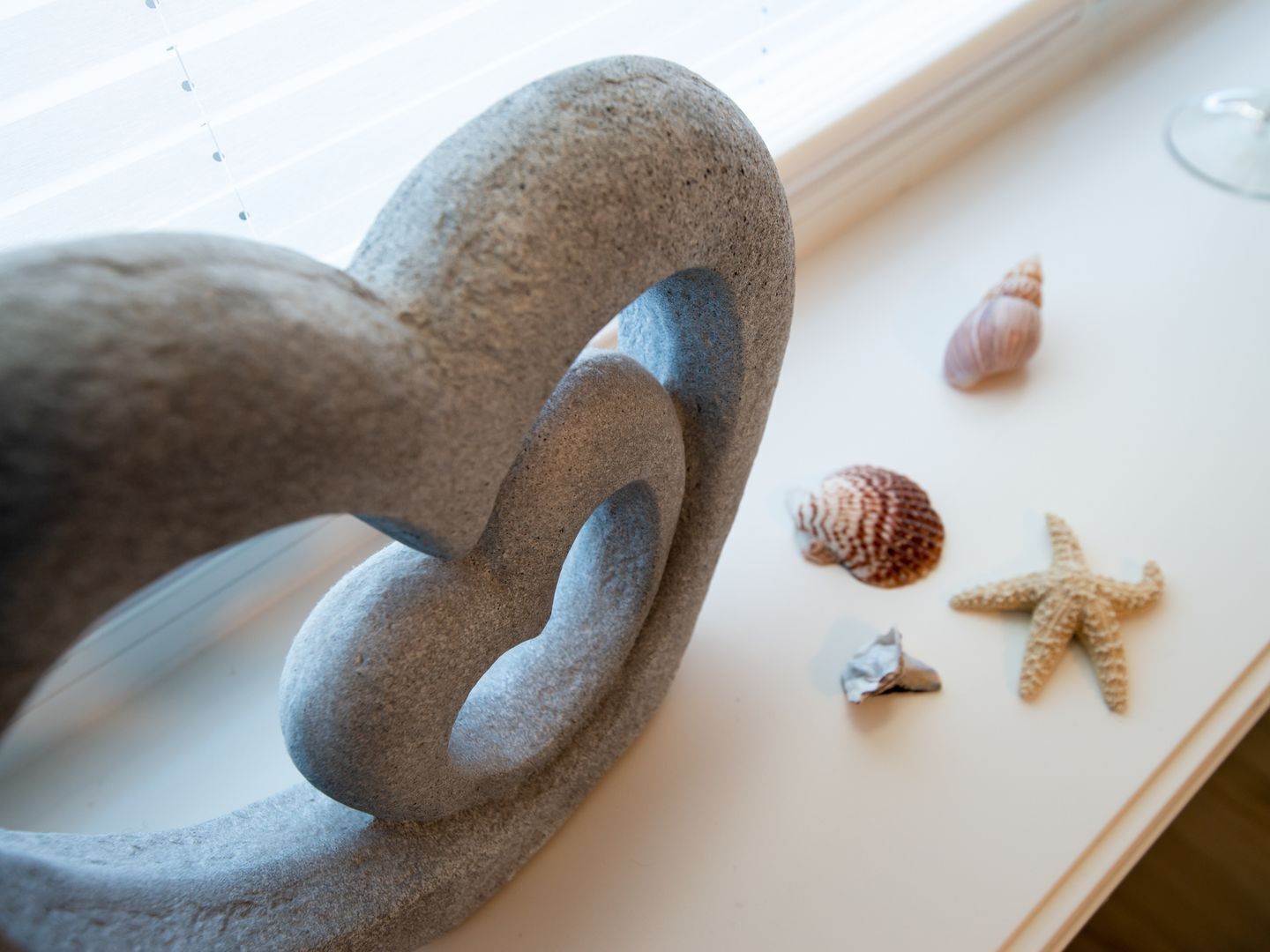 A stone sculpture with a looped design, a starfish, and a seashell on a white surface.