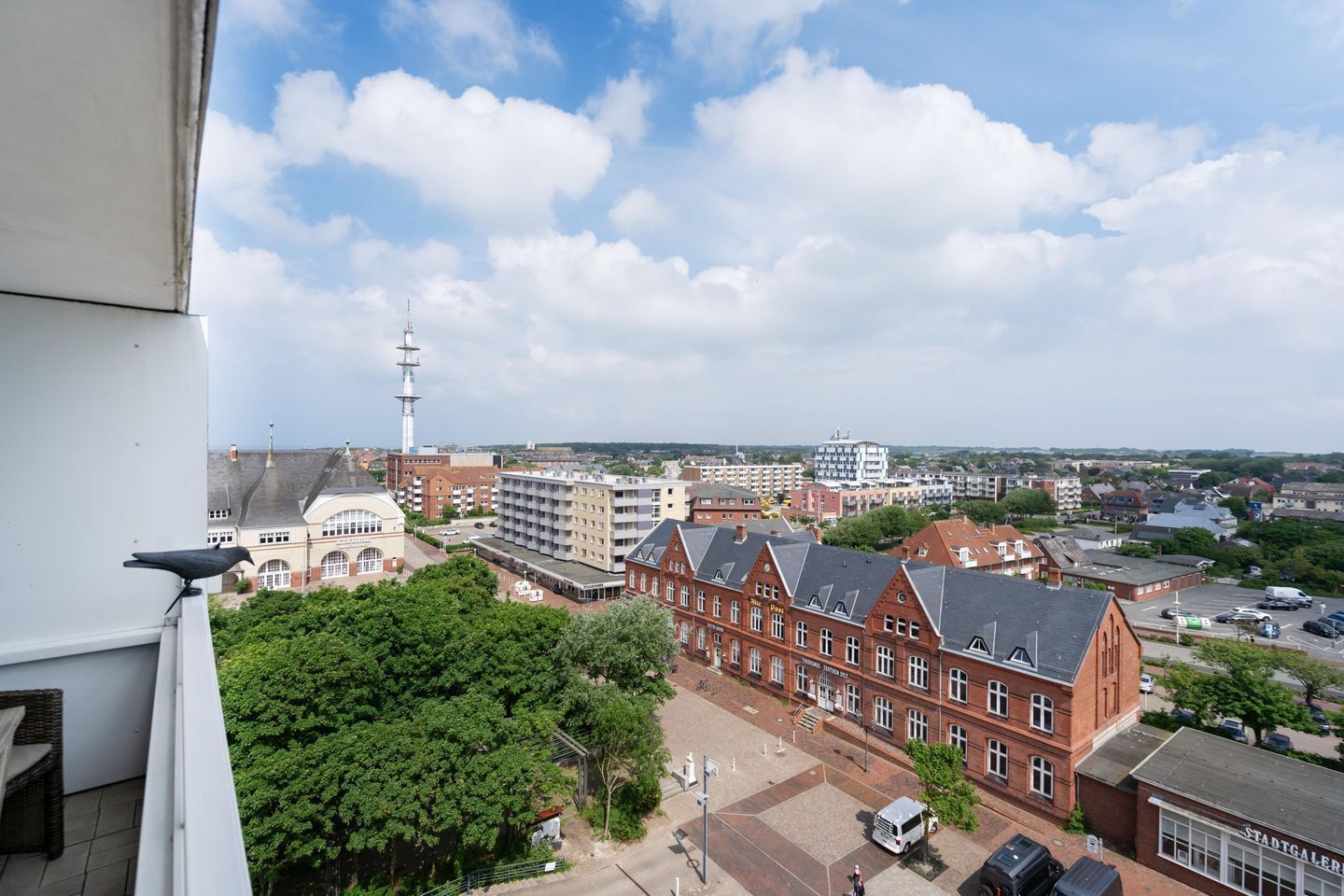 A cityscape with a prominent red brick building, a white tower, and a mix of residential and commercial structures.