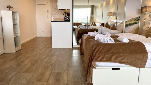 Une chambre d’hôtel moderne dotée d’un grand lit, d’un coin salon séparé, d’une kitchenette et offrant une vue sur la plage.