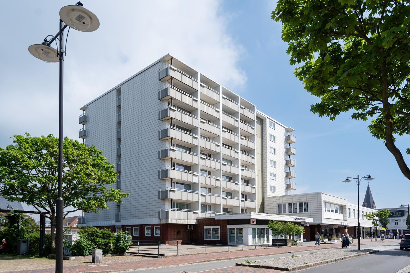 Een meerhoog gebouw met balkons, een voetpad en een straat met winkels.
