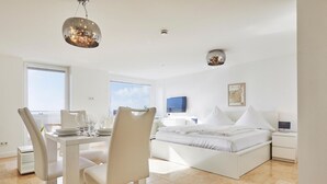 A modern bedroom with a large bed, a dining area with chairs, a TV, and a view of the sky. - Sea view I - Modern apartment, balcony with sea view, parking space, WLAN. (Sylt)
