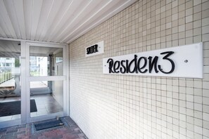 A building entrance with a glass door, a sign reading 'SITZER Residence 3', and a tiled wall. - Ocean View I - Modern apartment, balcony with ocean view, parking space, Wi-Fi. (Sylt)