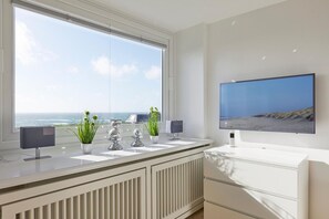 A modern bathroom with a large window, a flat-screen TV, and a radiator. - Ocean View I - Modern apartment, balcony with ocean view, parking space, Wi-Fi. (Sylt)
