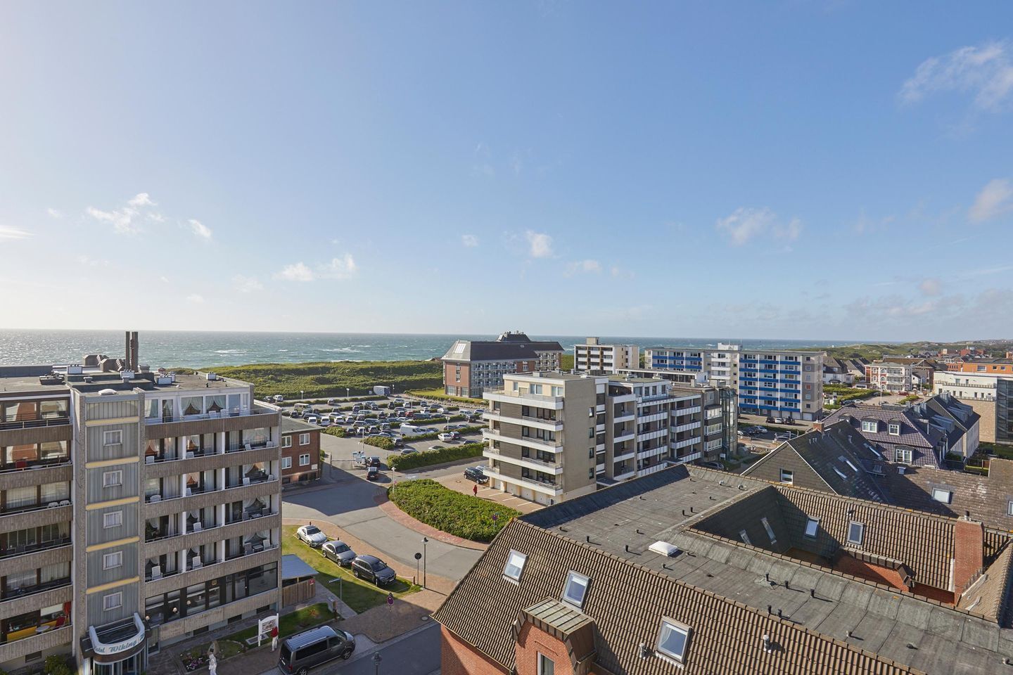 Zona residencial costera con edificios de apartamentos modernos, un estacionamiento y vista al mar.
