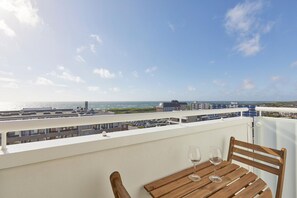A balcony with a wooden table and two wine glasses, overlooking a coastal area with buildings and a view of the sea. - Ocean View I - Modern apartment, balcony with ocean view, parking space, Wi-Fi. (Sylt)