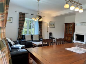 Een gezellige woonkamer met een houten eettafel, een bank en een open haard.