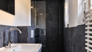 Um banheiro moderno com uma pia branca, chuveiro com porta de vidro e porta-toalhas.