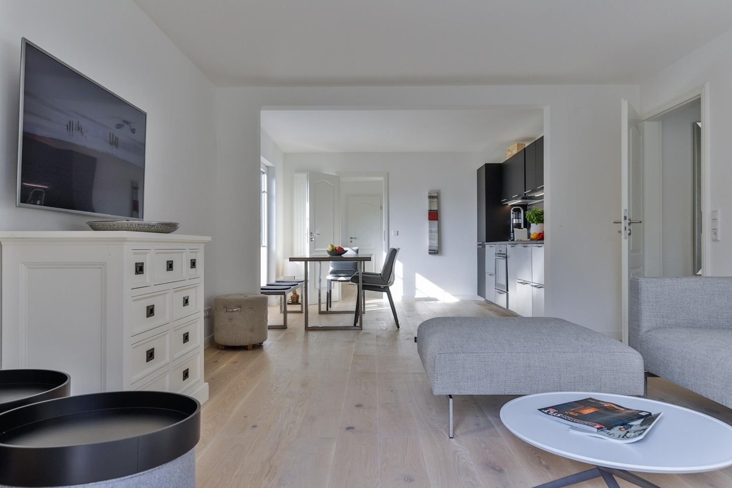 Un salon moderne avec un canapé gris, une petite table ronde et un téléviseur fixé au mur.