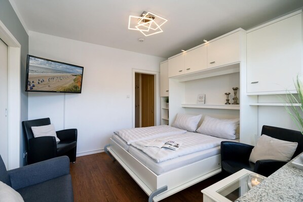 A modern bedroom with a bed, a desk, a chair, a TV, and a geometric light fixture.