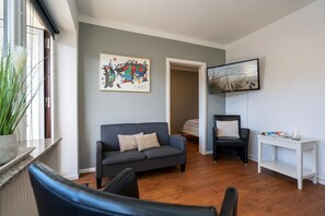 Un salon avec un canapé gris, un fauteuil noir, une table d’appoint blanche et un tableau accroché au mur.