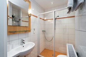 A modern bathroom with a glass shower enclosure, a white sink, and a mirror with a wooden shelf.