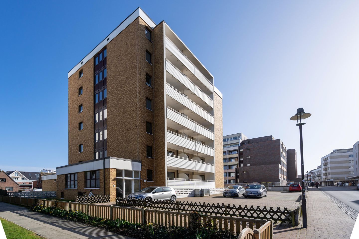 A multi-story building with a brick facade, a gated parking area, and a street with cars and pedestrians.