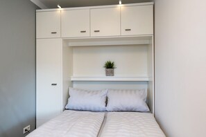 Une chambre à coucher avec un lit, deux oreillers, une étagère avec une plante et des armoires blanches.