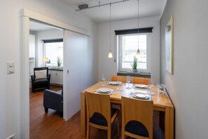 A dining area with a wooden table set for four, a black chair, and a view of the city through a window.