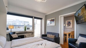 Moderni hotellihuone, jossa on kaksi sänkyä, ruokailutila ja taideteoksia seinillä.