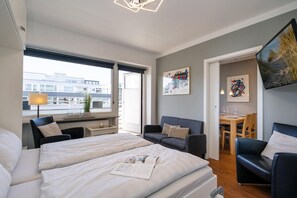 A modern hotel room with two beds, a dining area, and artwork on the walls.