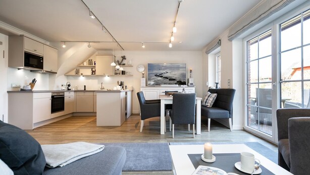 Una cocina moderna con una isla central, comedor con sillas, un sofá y un ventanal con vistas.