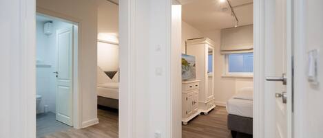 A modern bedroom with a bed, a dresser, and a nightstand. There is a bathroom with a toilet and a shower visible through an open door.