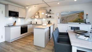 Una cocina moderna con armarios blancos, una isla central y una zona de comedor con mesa y sillas.