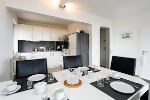 Een moderne keuken met witte kasten, een zwart aanrecht en een eethoek met een witte tafel gedekt voor vier personen.