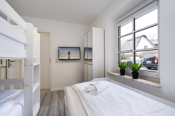 A bedroom with a bed, a wardrobe, a mirror, a window with plants, and a picture of a lighthouse. - Albatros, Ground Floor - Modern 3-room apartment that sleeps 4, with a terrace, garden, and parking space (Sylt)