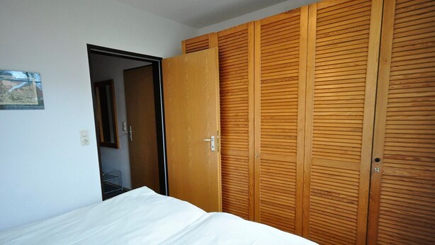 A bedroom with a bed, wooden wardrobe, and a door leading to another room. - Vacation apartment Warfstr. 3/3 - Wohnpark Werdum (Werdum)