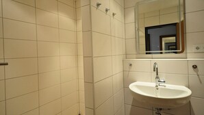 A bathroom with white tiles, a sink, a mirror, and a shower. - Vacation apartment Warfstr. 3/3 - Wohnpark Werdum (Werdum)