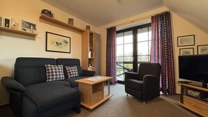 Una sala de estar con sofá, sillón, televisor y una ventana con cortinas.