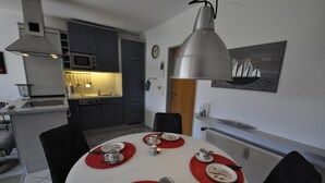 A dining area with a round table set for four, red placemats, and a modern kitchen in the background. - Vacation apartment Warfstr. 5/3 - Wohnpark Werdum (Werdum)