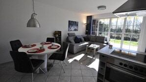 A modern kitchen with a dining area, a sofa set, and a large window providing a view of the outdoors. - Vacation apartment Warfstr. 5/3 - Wohnpark Werdum (Werdum)