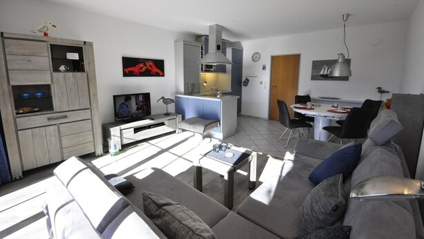 A modern living space with a sofa, TV, dining area, and kitchenette. - Vacation apartment Warfstr. 5/3 - Wohnpark Werdum (Werdum)