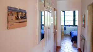 A hallway with a bed in the background, a door with a mirror, and a poster on the wall.
