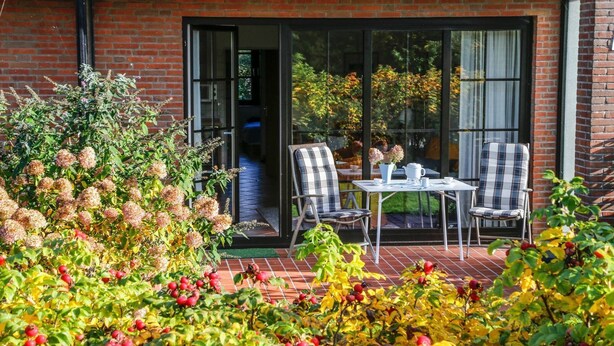 An outdoor patio with a brick floor, two chairs, a table, and a glass door leading inside.