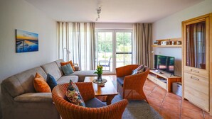 A modern living room with a sofa, two wicker chairs, a coffee table, and a TV.