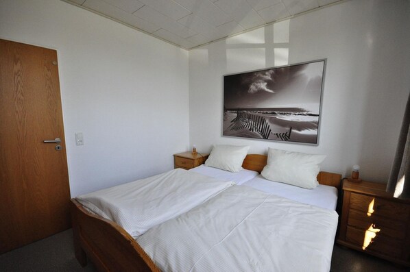 Cama doble con ropa de cama blanca, cabecera de madera y dos mesitas de noche con lámparas.