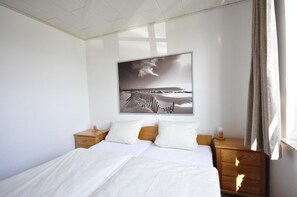 Un dormitorio con una cama, dos mesitas de noche, una lámpara de noche, un cuadro en la pared y una ventana con cortinas.