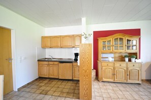 Cocina con armarios de madera, un lavamanos y una encimera. Una pared roja y una puerta se encuentran a la izquierda.