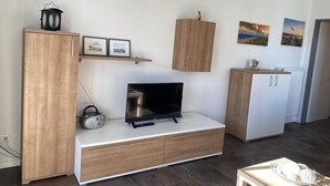 A modern living room with a flat-screen TV, wooden cabinets, and a shelf with framed pictures. - "Friesengeist" Werdum - Werdum residential park (Werdum)