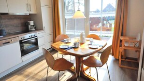 Une cuisine moderne avec des armoires blanches, un four encastré et un coin repas comprenant une table et des chaises en bois.