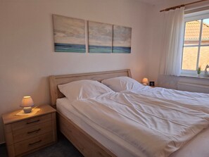 Une chambre à coucher avec un lit en bois, une literie blanche, une table de chevet avec une lampe et une fenêtre avec des rideaux.
