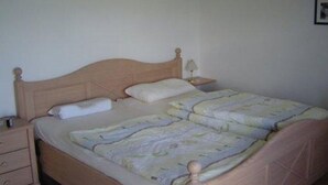 A single-bed room with a wooden headboard, a bedside table with a lamp, and a small drawer.