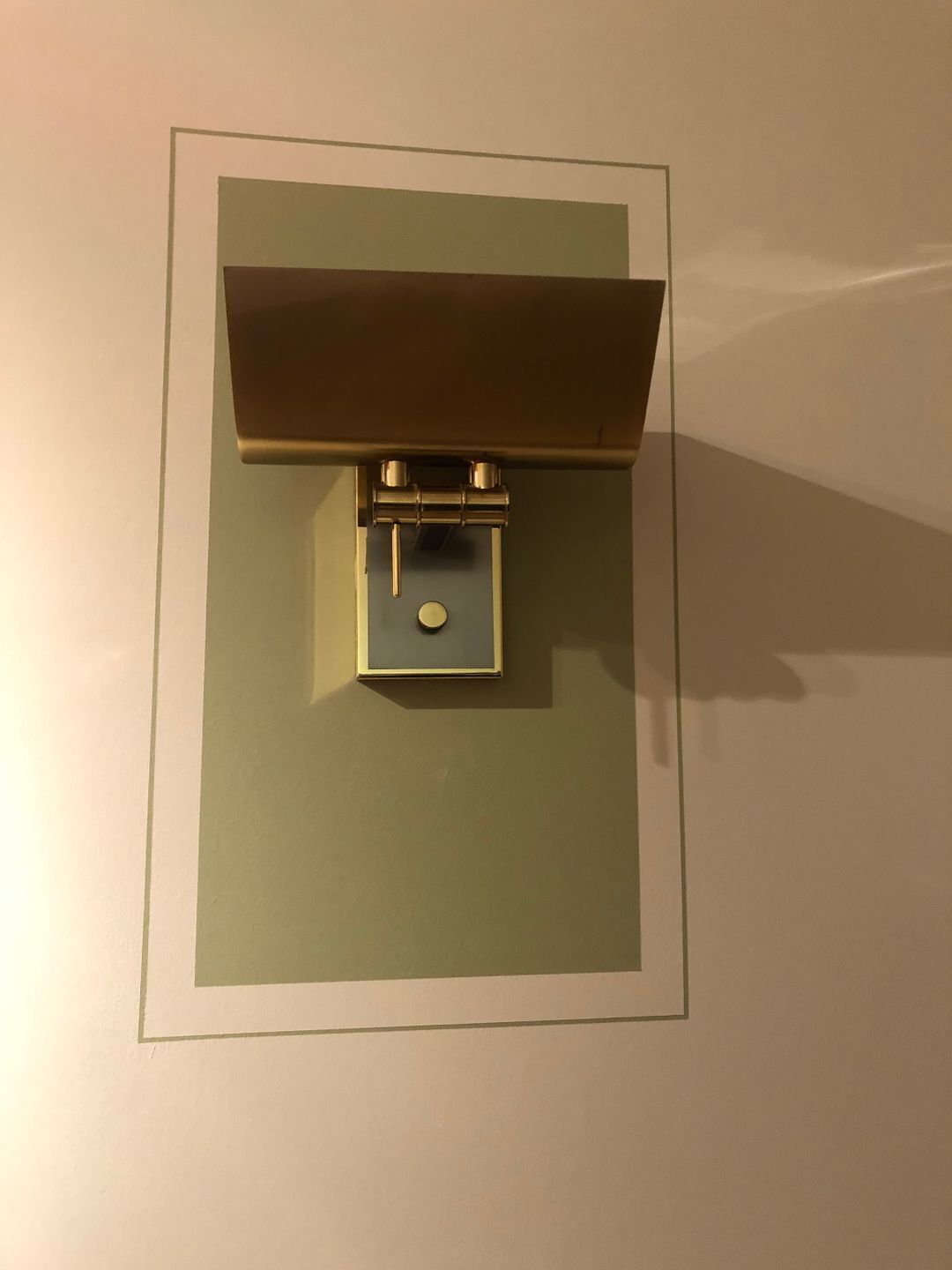 Een wandlamp met een rechthoekig voetstuk en een horizontale plank erboven.