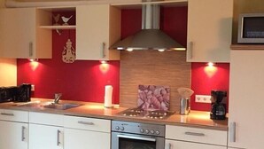 Een moderne keuken met witte kastjes, een rode accentmuur, een roestvrijstalen afzuigkap en een inbouwoven.