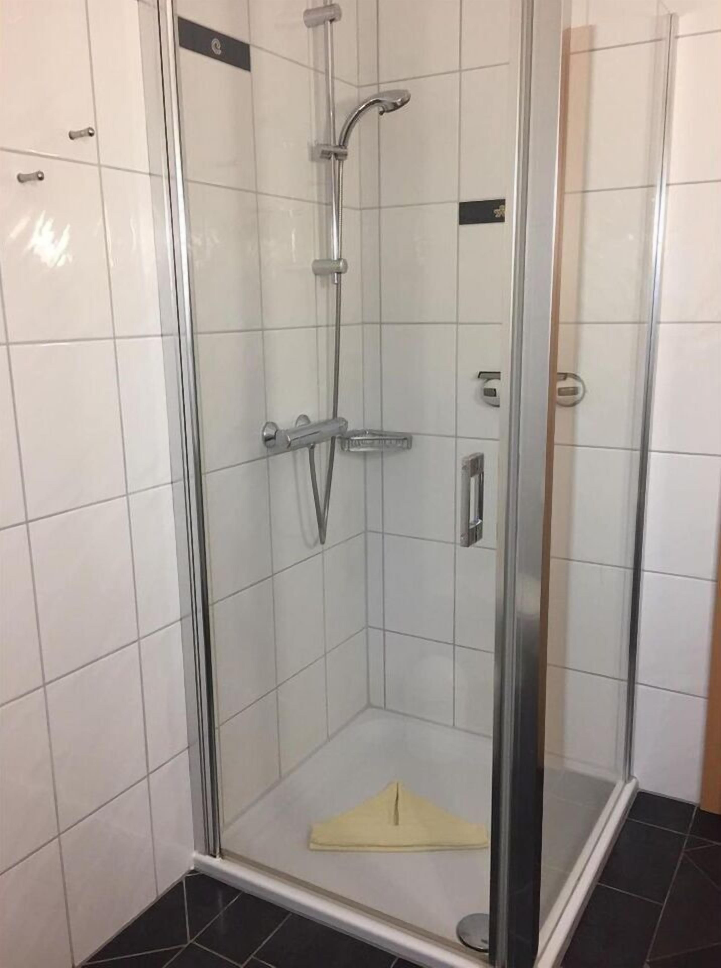 Un box de ducha con paredes de vidrio, un cabezal de ducha manual y un grifo empotrado en la pared.